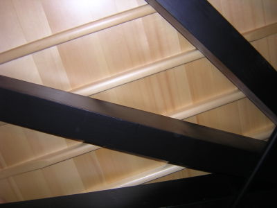 View from below of a 182-cm grand piano.  In order of distance from viewer:  softwood braces, tapered soundboard ribs, soundboard.  The metal rod at lower right is a humidity control device.